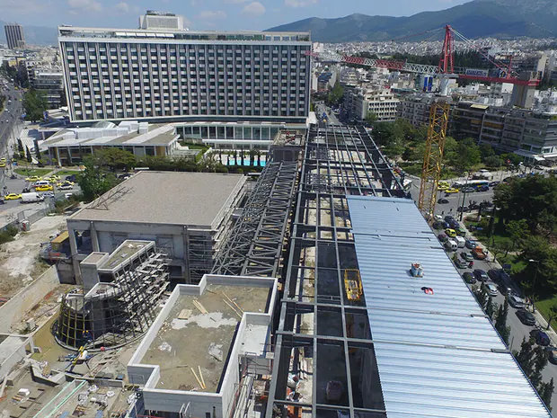 Aerial view of a building under construction with steel roof framing, among city blocks