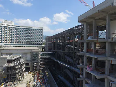 Building under construction between city blocks, a large multi-storey building behind