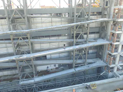 Sloping ramps and braced steel frames in front of a concrete wall with scaffolding