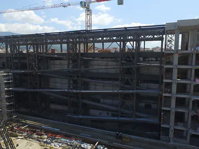 Tall steel frame between concrete walls, a tower crane above