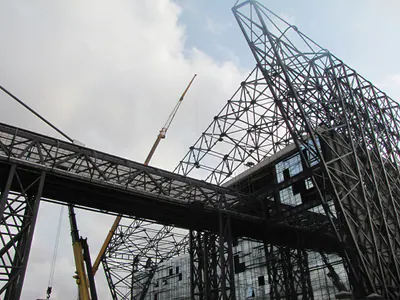 Steel space-frame roof rising over a walkway truss, seen from below