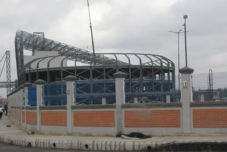 Building under construction with a curved steel roof frame behind a boundary wall