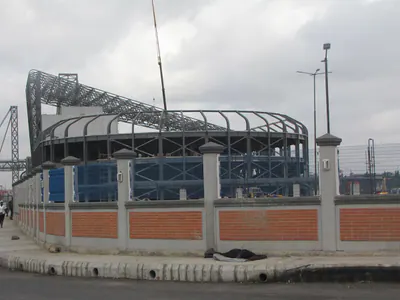 Building under construction with a curved steel roof frame behind a boundary wall
