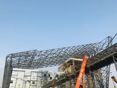 Sweeping steel roof frame over a building under construction, a crane beside it