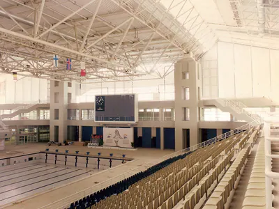 Indoor swimming hall with a steel roof, empty stands and a scoreboard