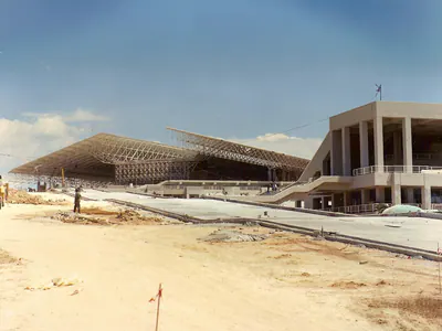 Building with a wide steel space-frame roof, seen across a construction site