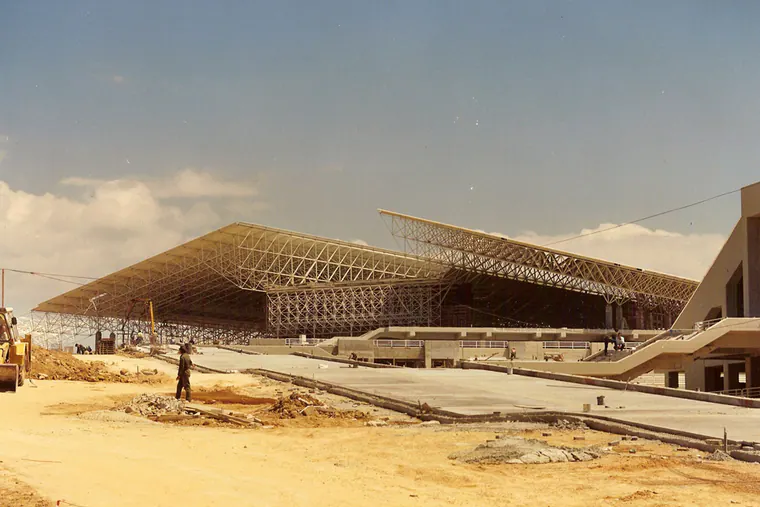 Large steel space-frame roofs seen across a sandy construction site