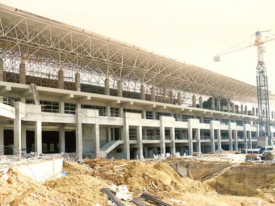 Long concrete building with a steel roof frame and a tower crane