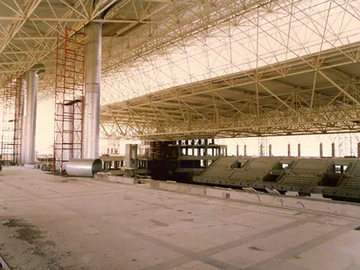 Tiered seating and large round ducts under a steel space-frame roof, during construction
