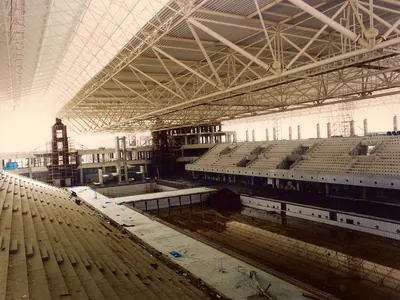 Stands and pool basin beneath a steel space-frame roof under construction