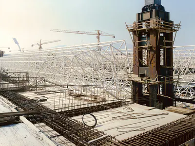 Tall tower in scaffolding, a steel space frame behind and reinforcement cages in front
