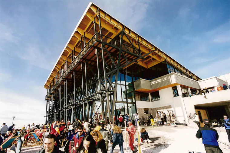 Ski centre building with a large pitched timber roof on steel columns, crowds in the snow