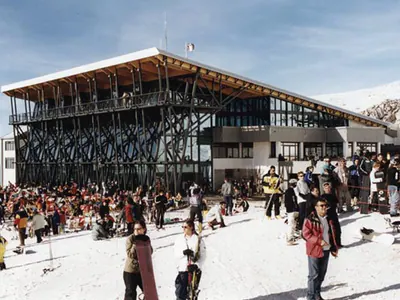 Visitors in the snow in front of a ski centre with a steel and timber frame
