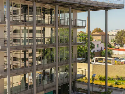 Steel-framed multi-storey building with a flat roof canopy, balconies and a ground-level garden