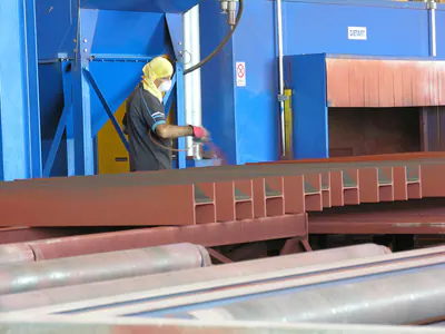 Worker in a protective mask and hood working on red-primed steel beams