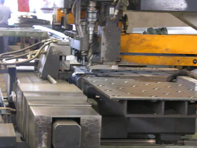Drilling head of a machine above a steel plate with drilled holes
