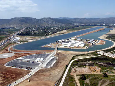 Aerial view of a long rowing lake with buildings and jetties on an island, mountains behind