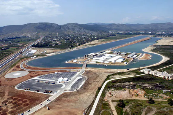 Aerial view of a long rowing lake with buildings and jetties on an island, mountains behind