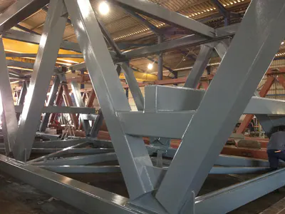 Grey-painted steel truss members inside a fabrication hall