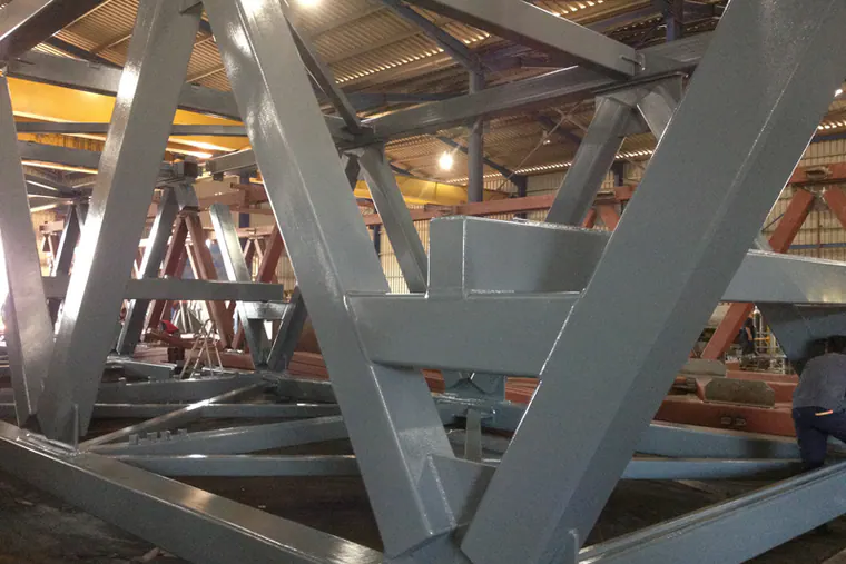 Grey-painted steel truss members inside a fabrication hall