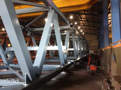 Long grey steel truss assembled in a fabrication hall