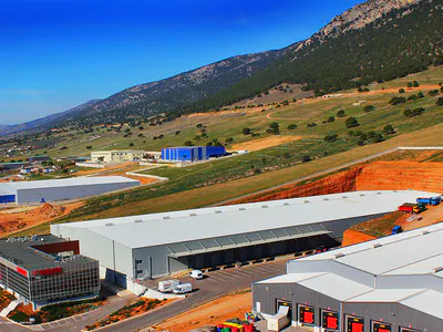 Office block and warehouses with loading docks below mountains, aerial view
